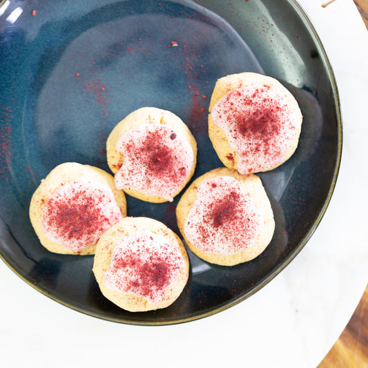 Five cookies with red sprinkles on a dark blue plate, placed on a wooden surface.